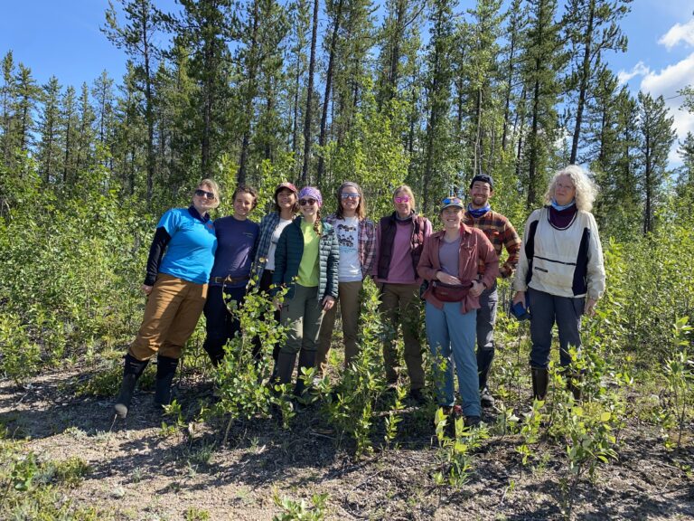 Nine scientists pose in front of some trees