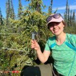 Katerina smiles and holds up calipers in a forest