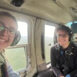 Two people smile inside a helicopter