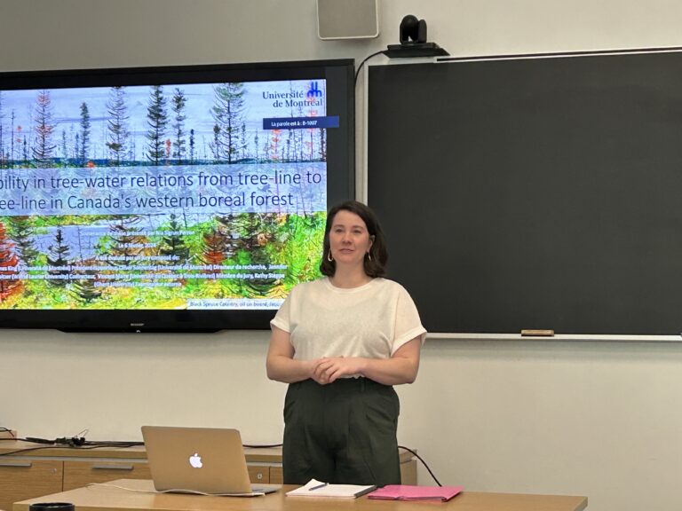 Nia stands in front of a projector with the title slide of her thesis
